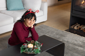 Naklejka premium Asian woman sitting at coffee table in living room wearing headband viewing evergreen wreath