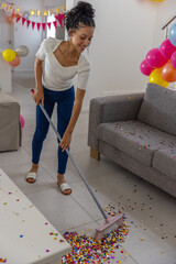 Obraz premium Teenage girl sweeping confetti with broom by gray couch in living room with balloons