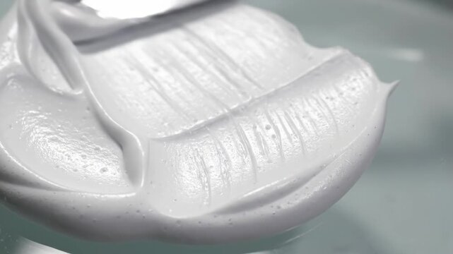 Creamy White Substance Being Swirled With A Metal Spatula On A Light Gray Surface Macro Shot