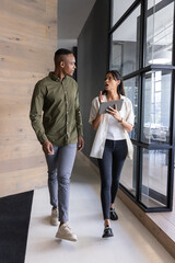 Fototapeta premium Diverse colleagues walking together conversing in office hallway holding tablet