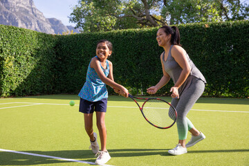 Obraz premium Asian mother and daughter swinging tennis rackets while playing on private, garden court