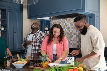 Diverse friends chopping fresh produce with chef knives on wooden kitchen island preparing salad © wavebreak3