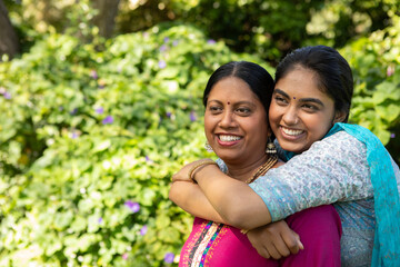 Indian mother and daughter hugging and smiling in garden with dupatta and jewelry, copy space © wavebreak3