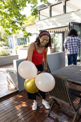 Obraz premium Diverse friends decorating deck by modern house with balloons, bunting flags under tree shadows