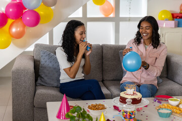 Obraz premium Diverse mom and teenage daughter inflating blue balloons in living room with birthday cake
