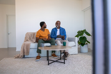 African american father and son chatting over tablet, coffee mugs in living room