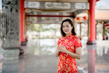 Fototapeta premium Elegant Asian woman in traditional red Chinese dress standing at a temple during Lunar New Year, expressing cultural heritage, celebration, and serenity