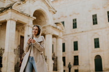 Woman walks in Malta and uses her phone near an old building