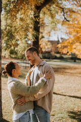 Fototapeta premium Couple enjoying a warm embrace in a vibrant autumn park on a sunny day
