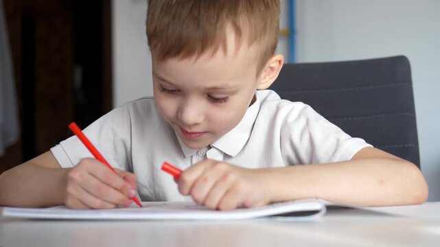 Close-up of a young boy writing or drawing with a pencil at a desk at home or school. Child focused on learning and doing homework. Concept of education, childhood development, concentration