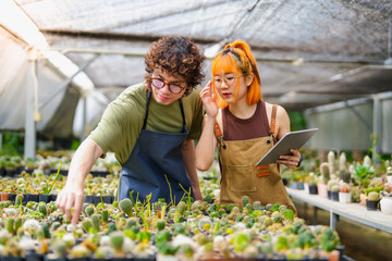 Fototapeta premium Young Asian Man and Woman Cactus Farm Owners Caring for Plants Together, Using Tablet for Small Eco-Friendly Business