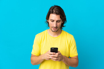 Young handsome man isolated on blue background sending a message or email with the mobile