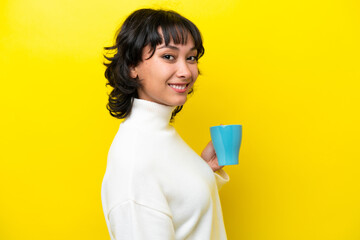 Young Argentinian woman holding cup of coffee isolated on yellow background smiling a lot © luismolinero
