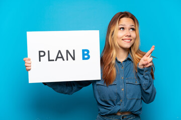 Teenager girl over isolated blue background holding a placard with the message PLAN B with fingers crossing