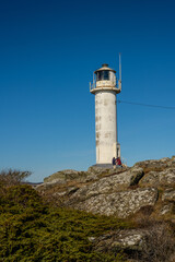 white coastal lighthouse standing on rocky terrain under clear sky.
