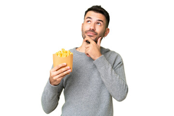 Young caucasian man holding fried chips over isolated chroma key background having doubts