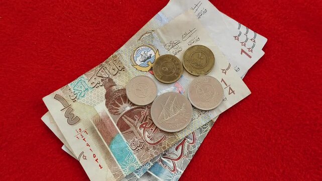 Bunch of kuwaiti dinar (KWD) currency notes and coins scattered on red table background. kuwait money, commerce, business, inflation, banking, savings, investment and economy concept. Closeup top view