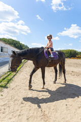 Little girl in safety helmet taking her first horse riding lesson with instructor