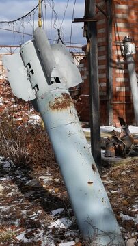 A projectile from a multiple launch rocket system has stuck into the ground, sticking out of the ground in the yard of a destroyed house in a Ukrainian village. Consequences of the shelling of a