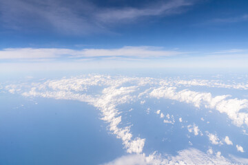 Obraz premium Clouds are visible above the vast ocean from an airplane window. The sky is mostly blue with some clouds. This scene shows the expanse of nature from a high point in the sky. High quality photo