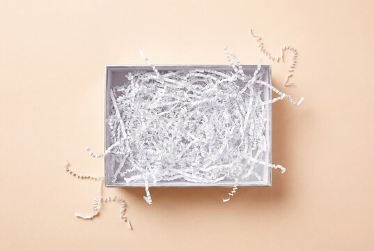 Open silver gift box with white shredded paper filler on pale peach background