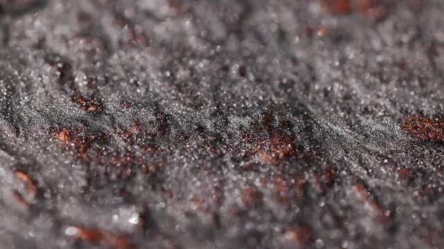 Detailed macro view of dark titanium paint with copper spots flowing slowly and forming uneven ridges to create a specialized sandy texture with radiant glitter particles shimmering 