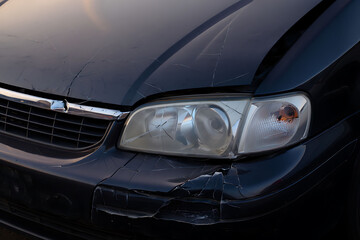 Damaged black car with cracked windshield and broken headlight closeup