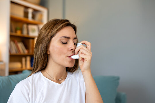 Young woman using a pressurized metered-dose asthma inhaler to treat respiratory issues or allergic reaction at home sitting on sofa managing asthma attack or chronic bronchitis symptoms
