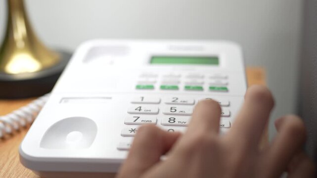 Close Up of Person Lifting White Telephone Receiver with Numeric Keypad on Wooden Surface