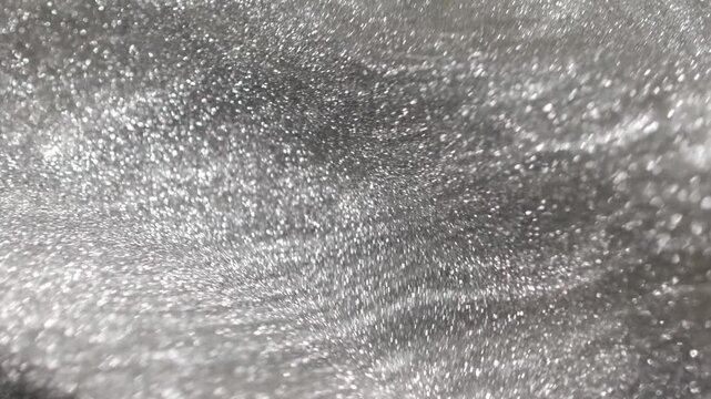Complex revolving shot of bright platinum paint specialized sandy texture and radiant glitter particles swirling on surface