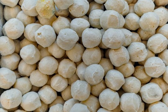 Overhead close-up shot of a large pile of freshly made, round, white fish balls, a popular Asian cuisine ingredient, viewed in a commercial setting, showcasing texture and culinary appeal.