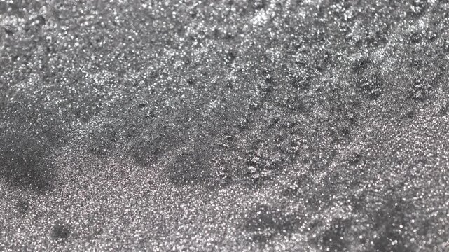 Detailed macro view of sparkling aluminium paint settling and separating into a complex webbed texture while shimmering with granular steel particles on abstract background