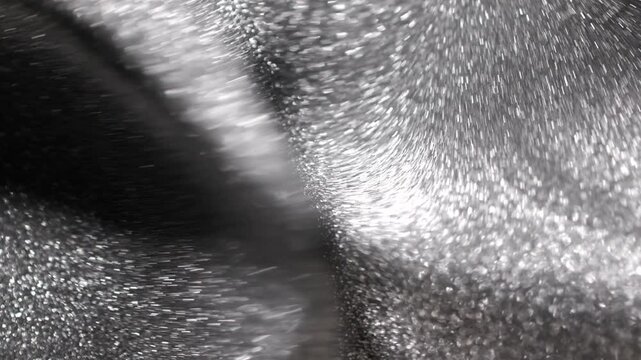 Undulating close-up of silver titanium paint forming deep elegant folds and waves while shifting and shimmering with radiant platinum particles on abstract metallic background