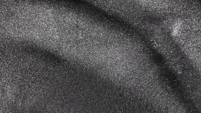 Elegant macro flow of dark titanium paint moving in smooth wave-like motion and dazzling particles spreading across a visually rich silver metallic surface on black background