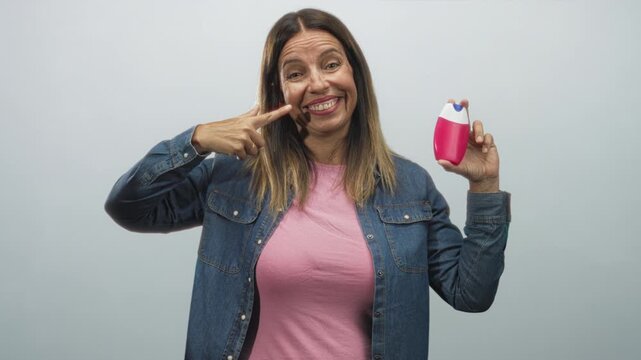 Woman points finger to teeth while holding pink toothpaste bottle in studio; confidence dental care.