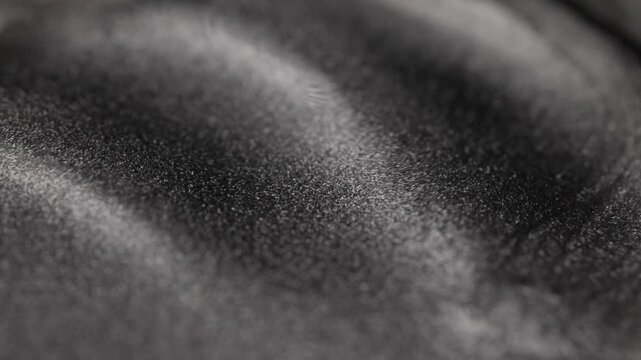Mesmerizing close-up of dark silver metallic fluid surface undulating gently with smooth waves and shifting light across the grainy texture, revealing glittering titanium particles 