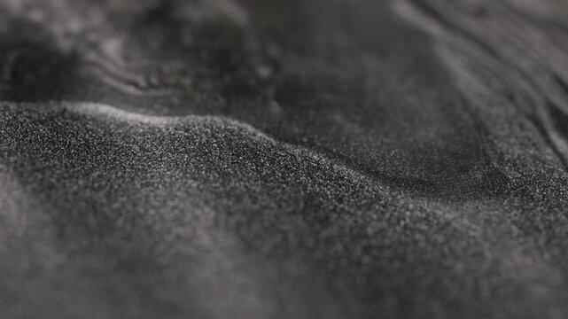 Mesmerizing close-up of dark platinum paint flowing slowly with a specialized sandy texture creating smooth undulating waves and highlighting glittering metallic particles on the surface