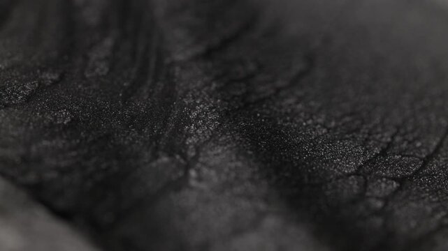 Dark titanium paint flowing slowly with a specialized sandy texture creating subtle ripples and highlighting radiant glitter particles on the surface