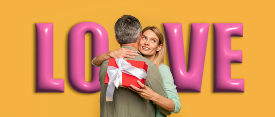 A man and a woman are hugging each other. The woman holds a small red gift box behind her. Bright letters spelling love are in the background. They appear happy and connected in this joyful moment.