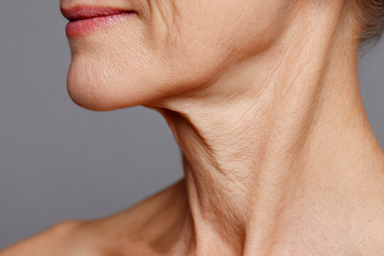 Profile of an elderly woman?s neck and jawline showing natural aging skin texture and subtle wrinkles against a neutral gray background