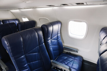 Obraz premium Empty airplane cabin interior with blue leather seats. Passenger seating row by window. Commercial aircraft economy class detail. Air travel comfort and transportation concept.