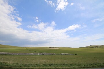 Obraz premium Rolling green hills and stone walls under a blue sky in the countryside.
