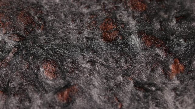 Dark platinum paint with bronze undertones slowly flowing and undulating, revealing a rough sandy texture and glittering particles