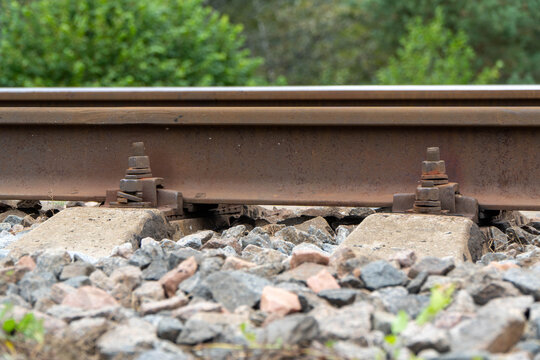 perspective of parallel rusty brown iron railway tracks fixed to reinforced concrete sleepers with heavy metal screw spikes and mounting clips over grey crushed stone ballast base