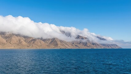 Clouds rolling over rugged mountains along the coastal landscape meeting the deep blue ocean coastline