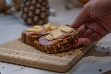 Hand placing cheese on ham sandwich on wooden cutting board