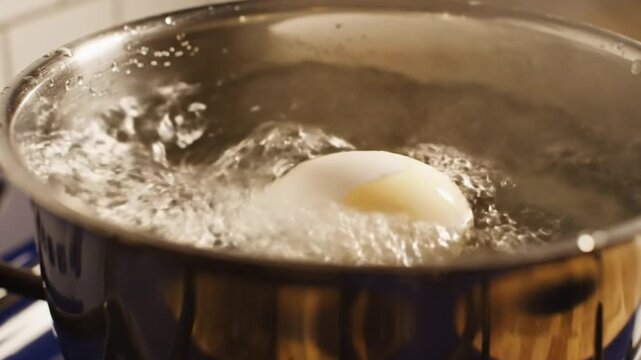 Boiling an egg in a stainless steel pot on a gas stove in close-up shot for cooking instructions