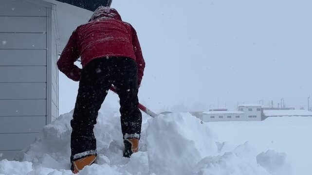 屋根から落ちた雪を寄せる作業をしている男性　豪雪　大雪　イメージ