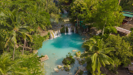 Fototapeta premium Drone aerial view of Cambugahay Falls in Siquijor, Philippines, featuring turquoise freshwater pools surrounded by lush tropical jungle and palm trees, showcasing a popular tropical travel destination