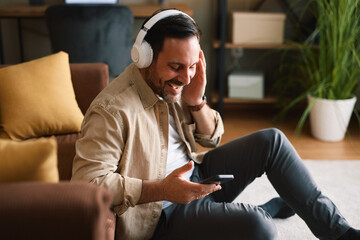 Obraz premium Man wearing headphones enjoying music on smartphone at home